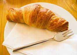 a cooked Croissant on a plate next to a fork and napkin.