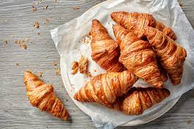 6 cooked croissants on a plate with one Croissant on the table.